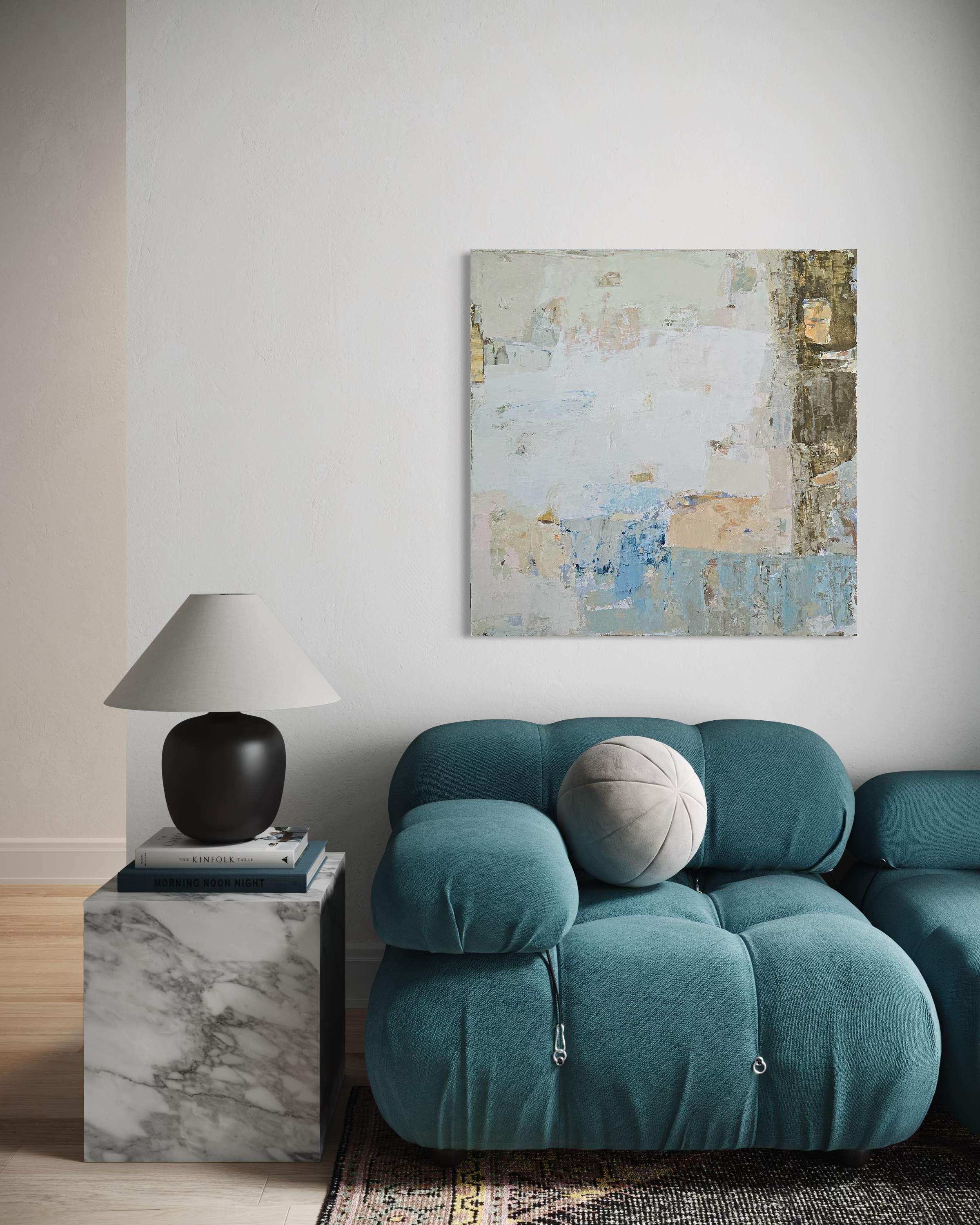 An abstract canvas painting with textured layers in blue, beige, and neutral hangs on a light gray wall above a teal tufted sofa with a white throw pillow. A black table lamp sits on a gray marble side table next to the sofa.